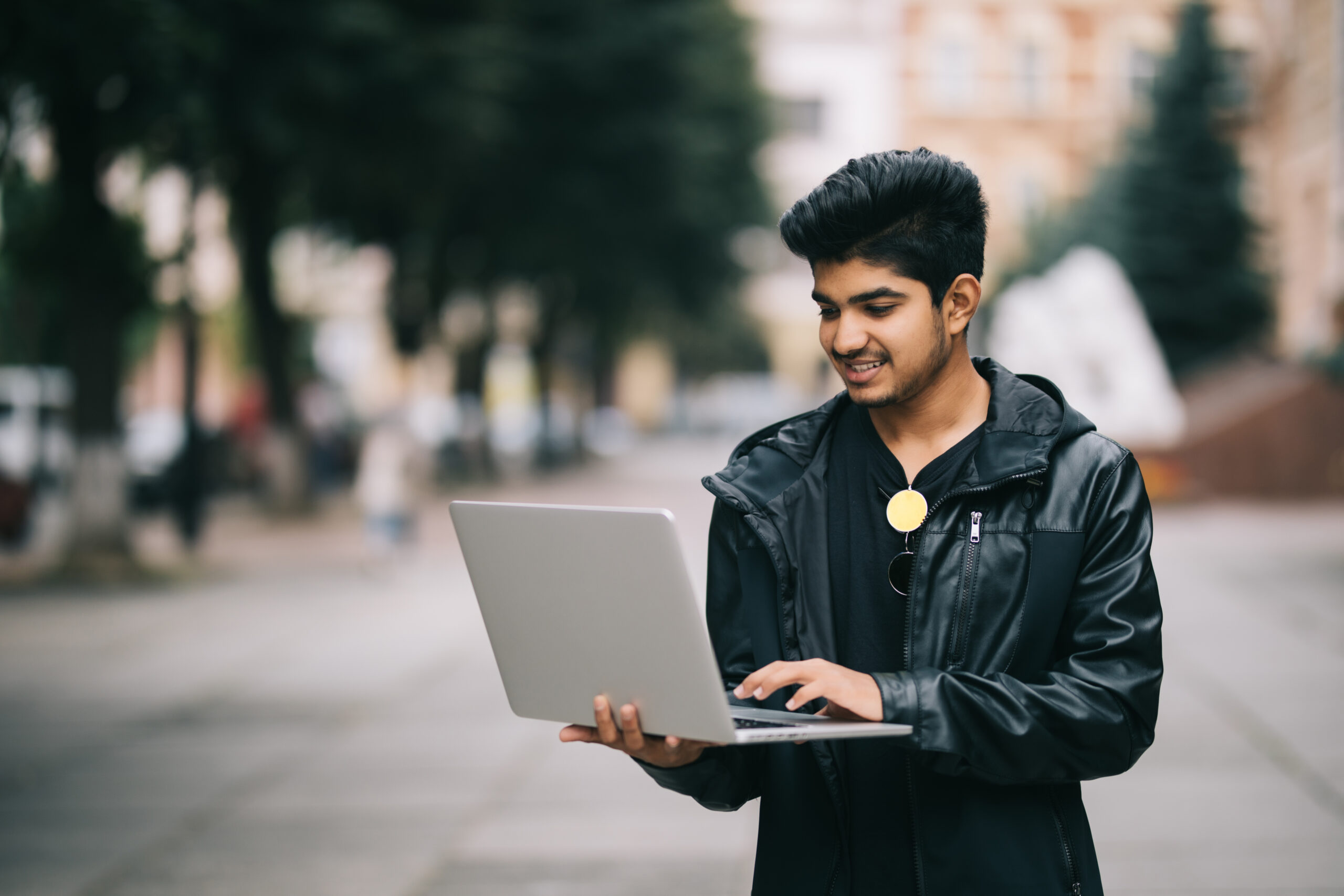 young indian man standing outdoor with laptop front scaled